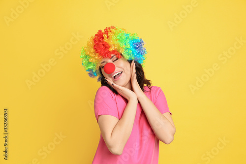 Joyful woman with rainbow wig and clown nose on yellow background. April fool's day