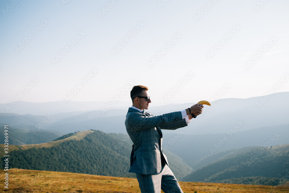 Secret agent in stylish suit standing in mountains,shooting with banana.
