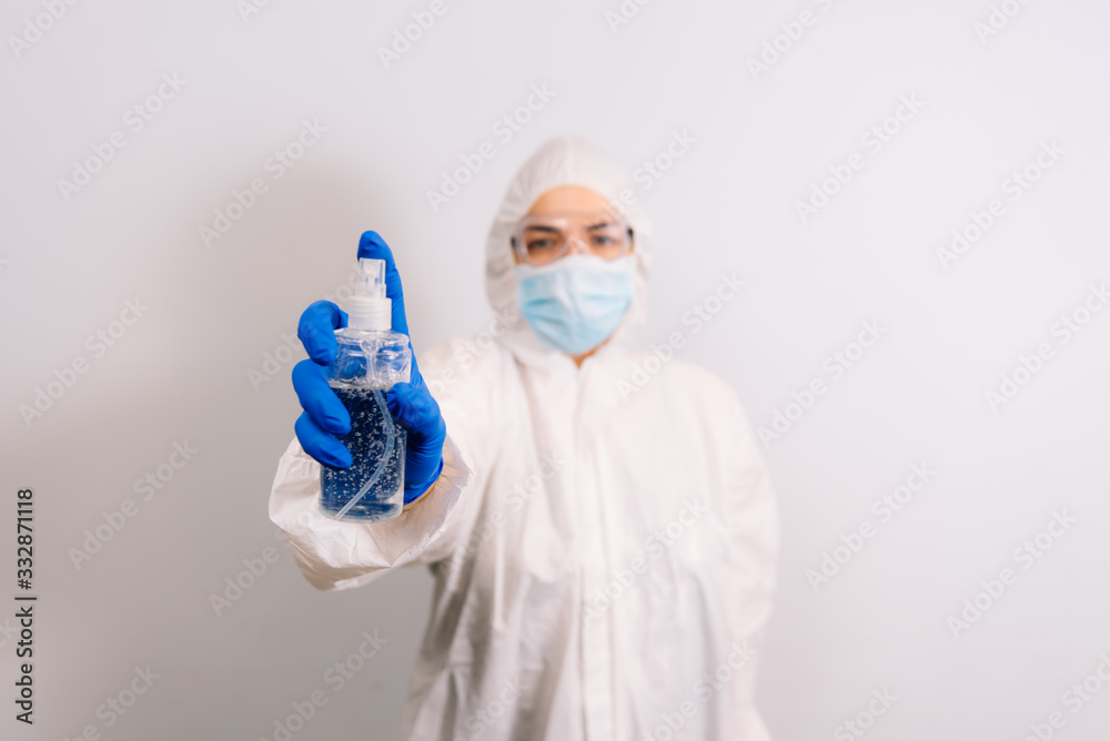 Hand sanitizer against germs and viruses. Contains alcohol. A doctor hand wearing a blue glove is holding an bottle. Blurred doctor in the background. Stop coronavirus. COVID-19. Hand sanitizer against germs and viruses. Contains alcohol. A doctor hand wearing a blue glove is holding an bottle. Blurred doctor in the background. Stop coronavirus. COVID-19.
