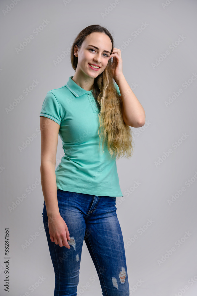 Vertical photo of a pretty girl with long beautiful hair with a smile in a turquoise blouse and blue jeans on a white background. Vertical photo of a pretty girl with long beautiful hair with a smile in a turquoise blouse and blue jeans on a white background.