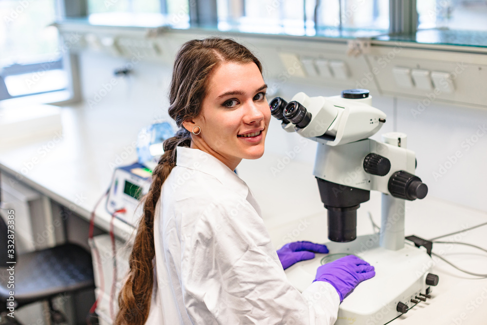 Scientists seats near microscope and looks over Scientists seats near microscope and looks over
