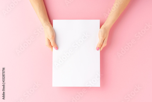 Woman’s hands holding empty white paper sheet on pink background. Close up
