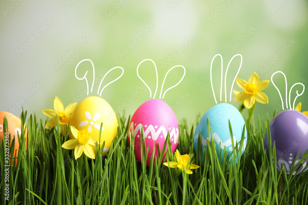 Bright Easter eggs with cute bunny ears and flowers in green grass