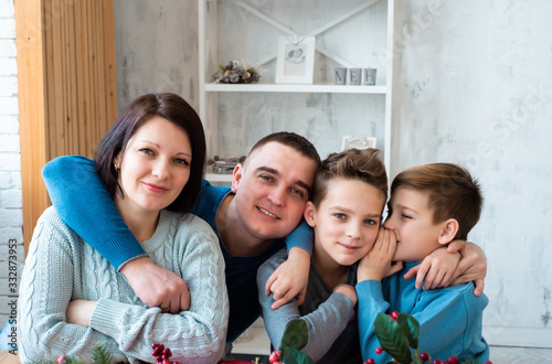 Portrait of beautiful happy family at home. Smiling people hugs together. Mother  father and 2 kids sitting at the kitchen. Two brothers having secret  parents feeling happy and look into the camera. 