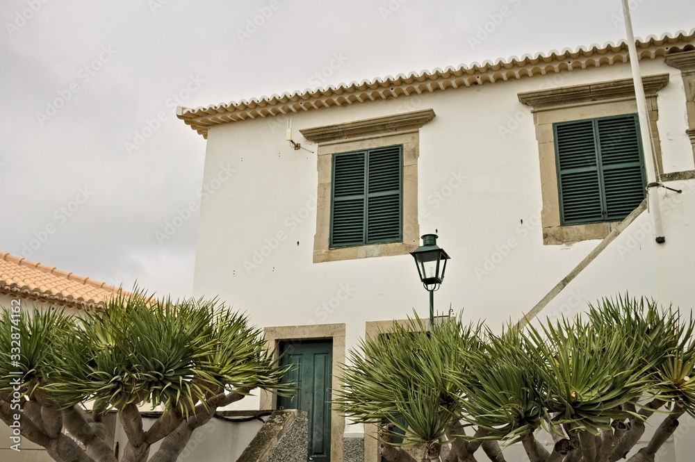 White facade of an old house with an isolated lamppost and plants in the garden (Madeira, Portugal, Europe)
