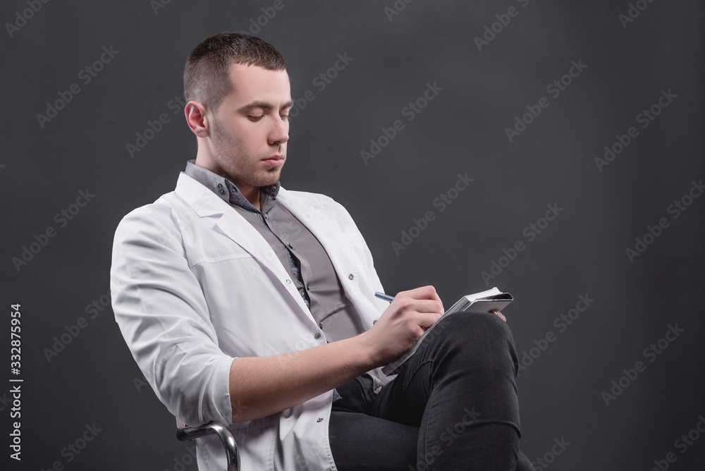 Naklejka premium Young, pretty man in a medical coat on a gray background. The concept of medical education and medical activity