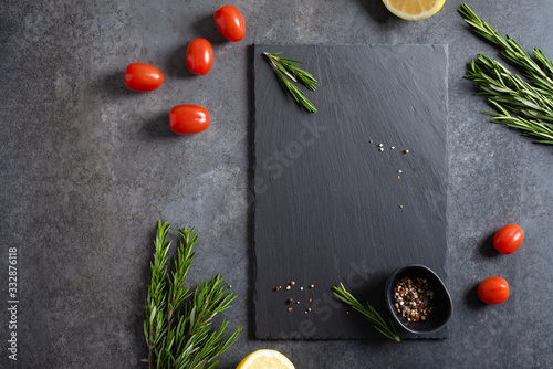 Empty black stone board and ingredients on dark background. Free space for text and brand product. Cherry tomatoes, rosemary, lemon and spicies phrame. Top view, flat lay. Restaurant food background photo