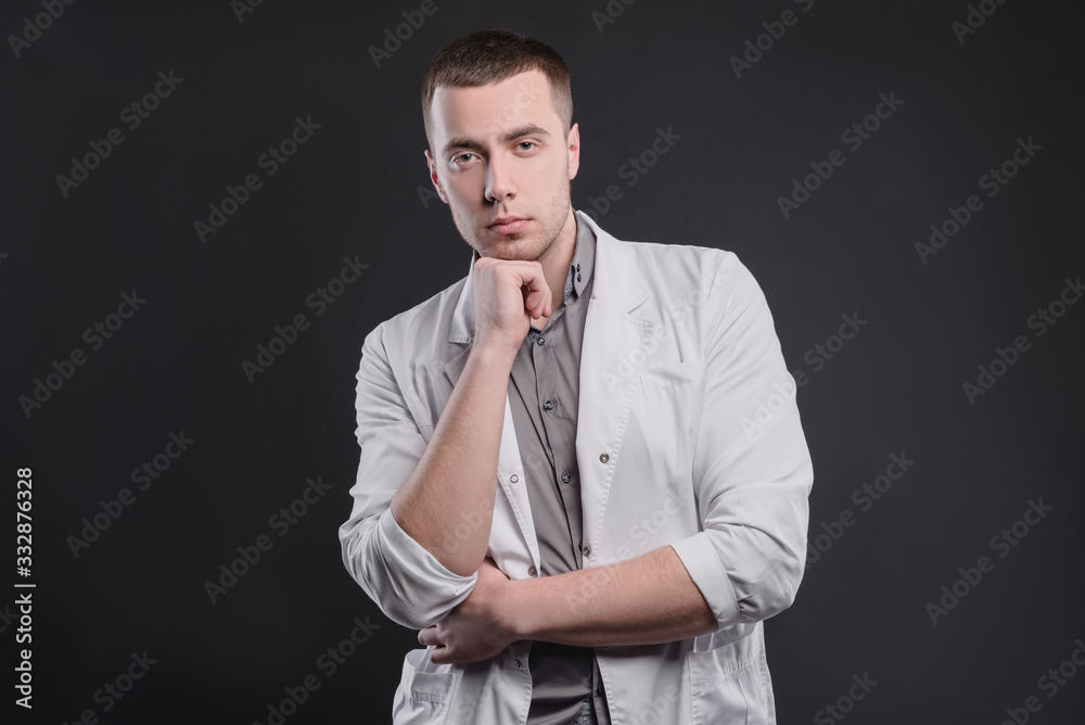 Young, pretty man in a medical coat on a gray background. The concept of medical education and medical activity Young, pretty man in a medical coat on a gray background. The concept of medical education and medical activity