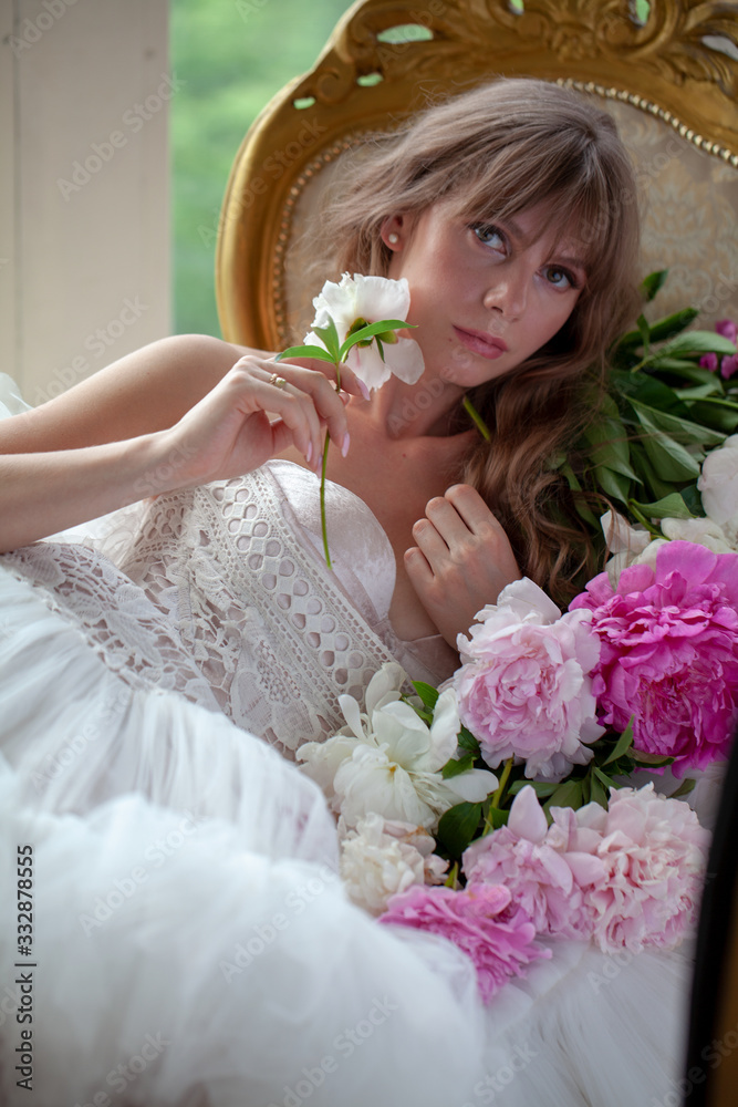 Bride in beautiful dress lying on sofa whit peonies in white studio interior. Romantic wedding style shot with sun light Bride in beautiful dress lying on sofa whit peonies in white studio interior. Romantic wedding style shot with sun light