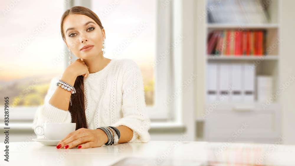 Slim young woman sitting in home interior and white wooden table of free space for your decoration.Blurred background of window.