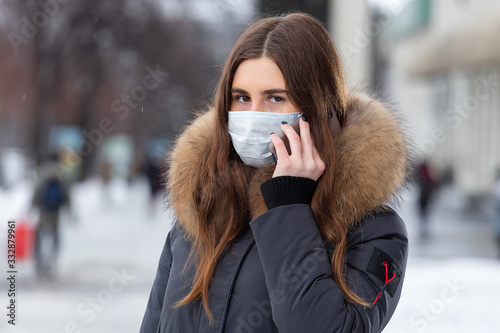 A young girl stands near the road and talking on the smartphone in a medical mask. Protection against virus outbreaks, flu and air pollution from cars in the city © simikov