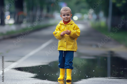 child in a raincoat plays outside in the rain / seasonal photo, autumn weather, warm clothes for children