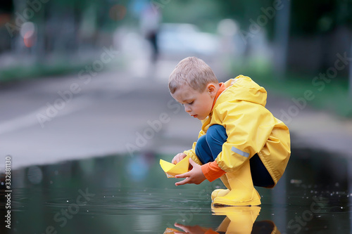 a boy plays boats in a puddle   childhood  walk  autumn game in the park  a child on a walk