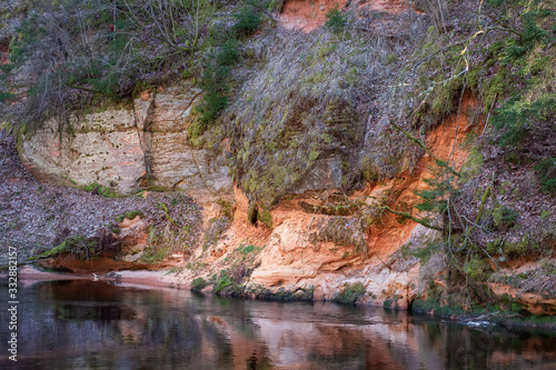 Sandstone rock wall at river with forest, rock reflection in river water, Gauja national park, Latvia. River Brasla