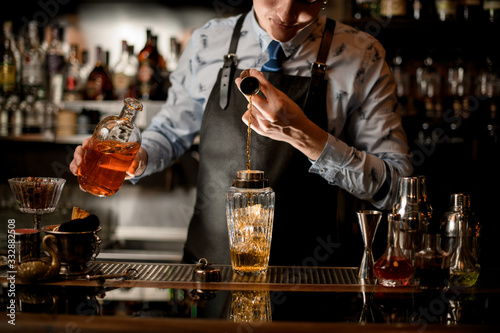 Professional barman using beaker pours drink into glass shaker