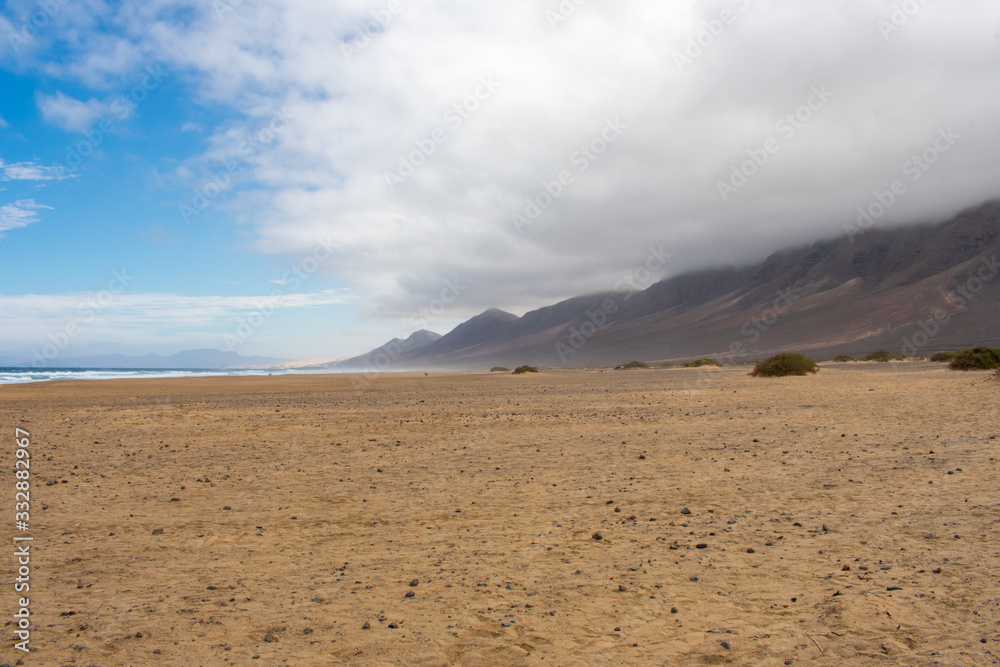 Playa De Cofete Canary Islands, Fuerteventura, Spain. Beach, mountains and Atlantic Ocean against cloudy sky 