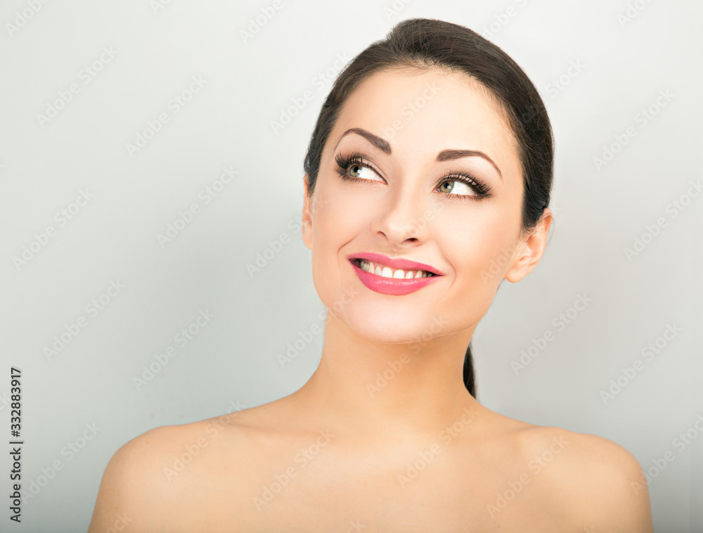 Beautiful woman with healthy clean face skin looking up and thinking with toothy smile. Correction eyebrows shape. Dental perfect health. Studio blue background. Closeup Beautiful woman with healthy clean face skin looking up and thinking with toothy smile. Correction eyebrows shape. Dental perfect health. Studio blue background. Closeup