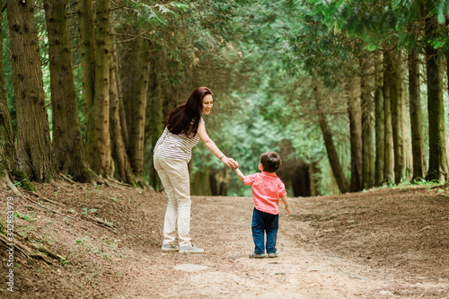 Backview of Mother walking with cute son in summer park. Happy woman with cheerful little boy outdoors