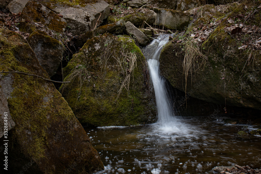 A beautiful small waterfall in a thicket of forest on high hills among huge boulders covered with moss A beautiful small waterfall in a thicket of forest on high hills among huge boulders covered with moss