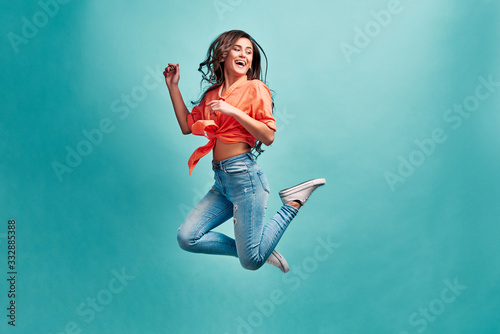 Photo of a beautiful girl bouncing on a blue background with happiness and looking away. The concept of joy, pleasure, youth and beauty.