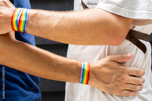 Two young men hugging each other with an lgtb flag bracelet on the street