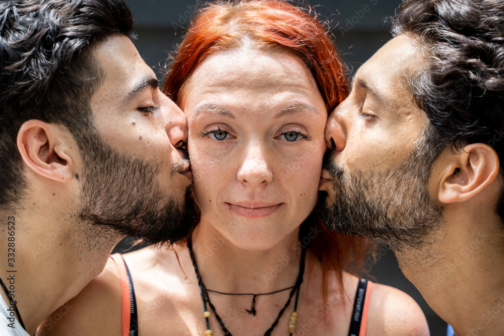 Two young boys of different ethnicities kissing on the cheek of a girl standing in the middle Two young boys of different ethnicities kissing on the cheek of a girl standing in the middle