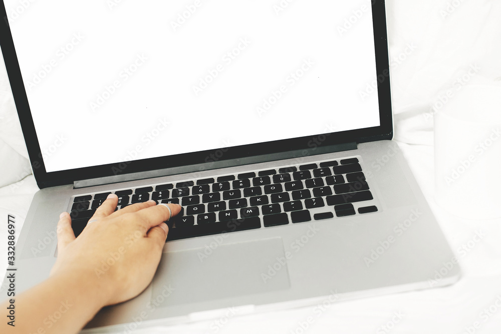 Person using laptop with blank white screen on white cozy bed, copy space. Shopping online from bed, hand on keyboard. Working online from home. Mockup. Freelance concept. Staying home Person using laptop with blank white screen on white cozy bed, copy space. Shopping online from bed, hand on keyboard. Working online from home. Mockup. Freelance concept. Staying home