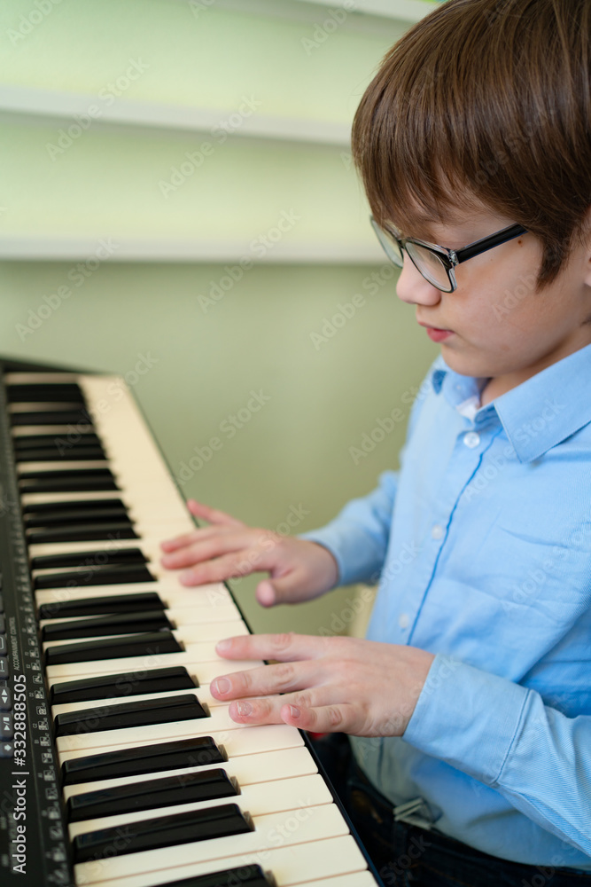 Fototapeta chłopiec w okularach uczy się grać na syntezatorze.