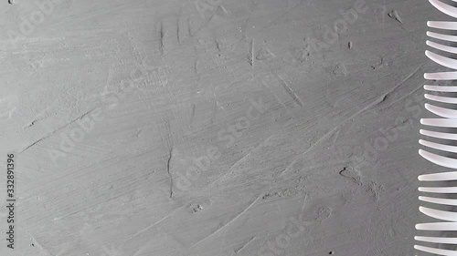 White plastic disposable forks slowly slide out from the edge of the frame against the gray cement surface