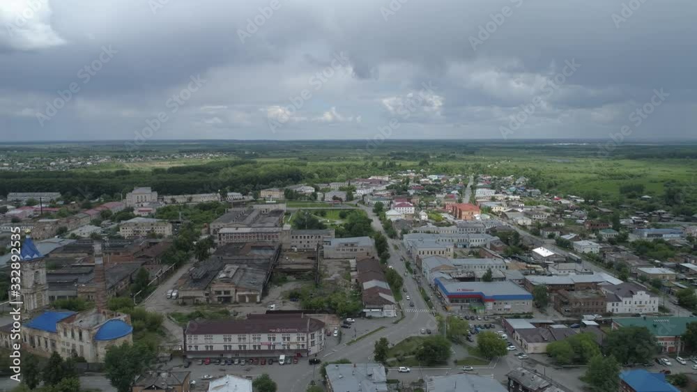 Aerial view of ruined church near the factory in city with low houses. Out of town forests. Summer day, cloudy. Irbit city, Sverdlovsk region, Russia