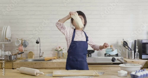 cute little asian girl dancing and smiling while baking in kitchen. happy daughter prepare cake diy for happy mother's day. cheerful kid child holding dough for cookie in hand having fun face camera.