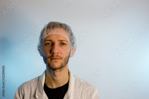 An adult male dressed in a white lab coat with a hair net on. Ready to work in a clean room or laboratory