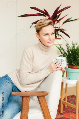 Thoughtful mature woman sitting in cafeteria or at home holding coffee mug while looking away. Middle aged woman drinking tea while thinking. Relaxing and thinking while drinking coffee.