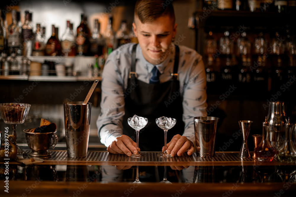 bartender holds two glasses with ice on bar counter. bartender holds two glasses with ice on bar counter.