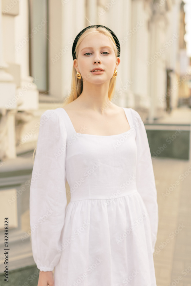 Cute blonde girl smile and relaxing on the street. Wearing summer fashionable linen clothes.