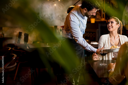 Smiling young female friends at a restaurant with waiter serving dinner photo