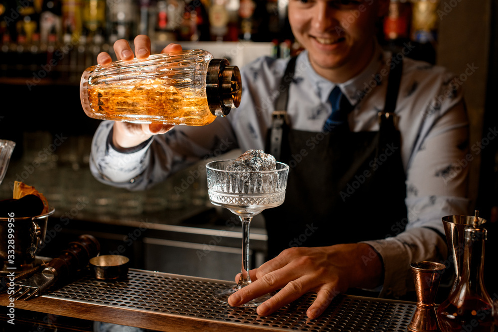 young smiling bartender carefully pours drink from shaker into glass.