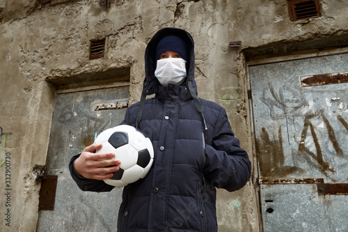 concept of epidemic and quarantine - a boy with a face mask and a ball alone on the street in the city