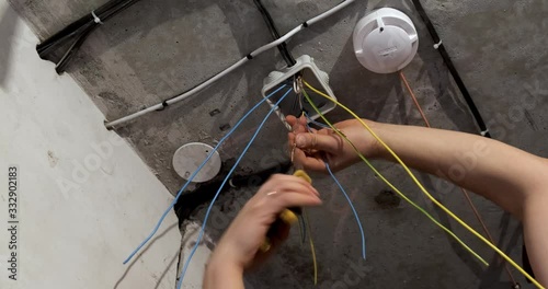 Man twists electric wires with pliers, construction, repair work in room, new electrical wiring is stretched out under ceiling, building is repaired, electrical work, long wires stick out from ceiling