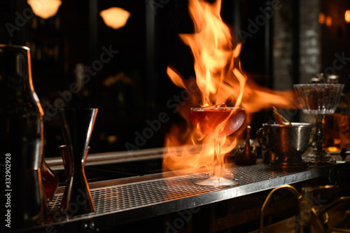 glass with cocktail on fire stands at bar counter.
