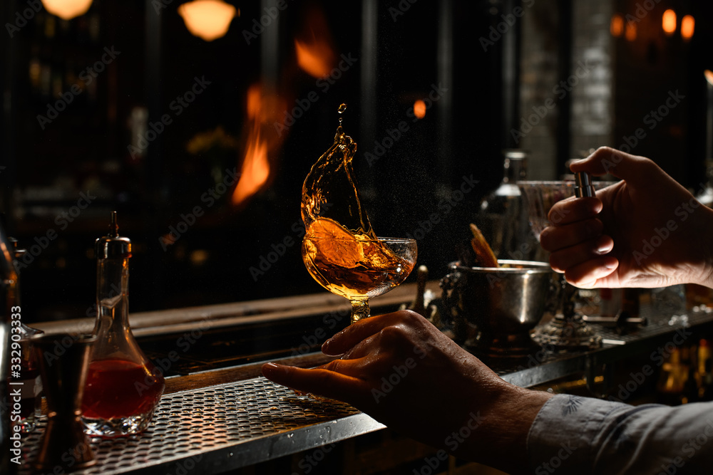 Naklejka premium bartender holds by hand glass with splashed alcohol drink and spray to it.