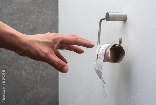 A hand reaching for an empty toilet paper holder (concept toilet paper finished)