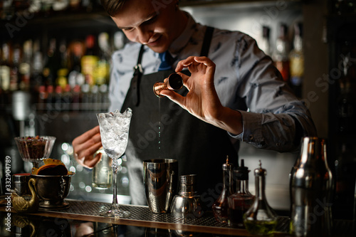Young smiling bartender professionally pour drink to shaker using beaker.