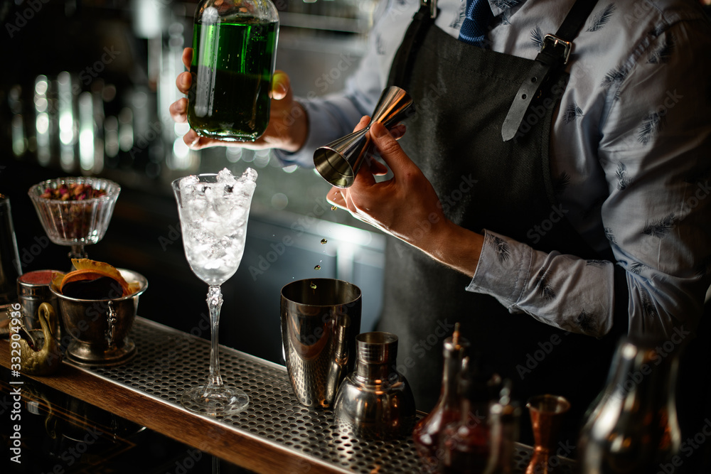 bartender in black apron begins to prepare green alcoholic cocktail
