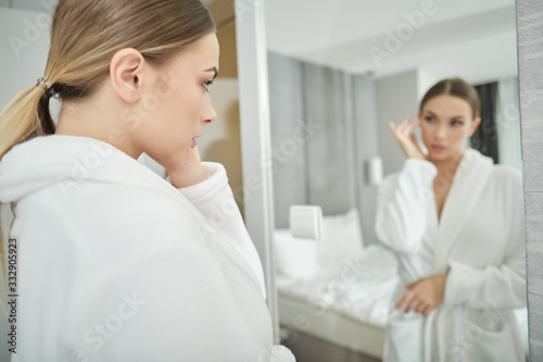 I am beautiful. Portrait of confident young woman looking at mirror with satisfaction while standing in bathrobe at home. Body care concept