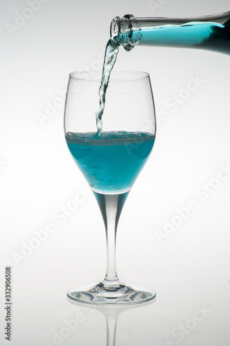 a bottle pouring blue liquor into a glass, isolated on white background