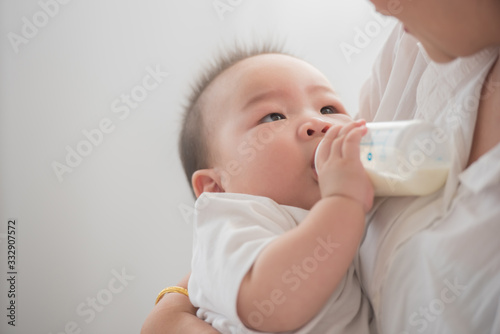 mother holding and feeding baby from milk bottle.portrait of cute baby being fed by her mother using bottle. loving woman giving drink milk to her son. mother feeding newborn baby from bottle at home