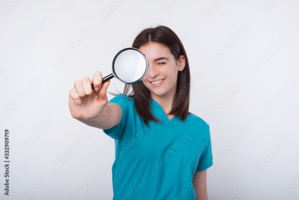 Photo of young woman doctor looking trough magnifying glass over white background Photo of young woman doctor looking trough magnifying glass over white background