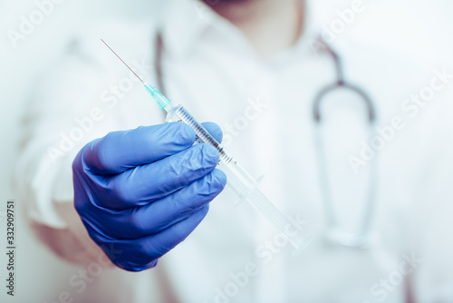 detalle de una jeringuilla en la mano de un doctor con guantes azules y fondo desenfocado