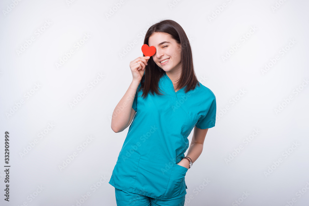 Portrait of happy smiling young doctor holding red paper heart over her eyes Portrait of happy smiling young doctor holding red paper heart over her eyes